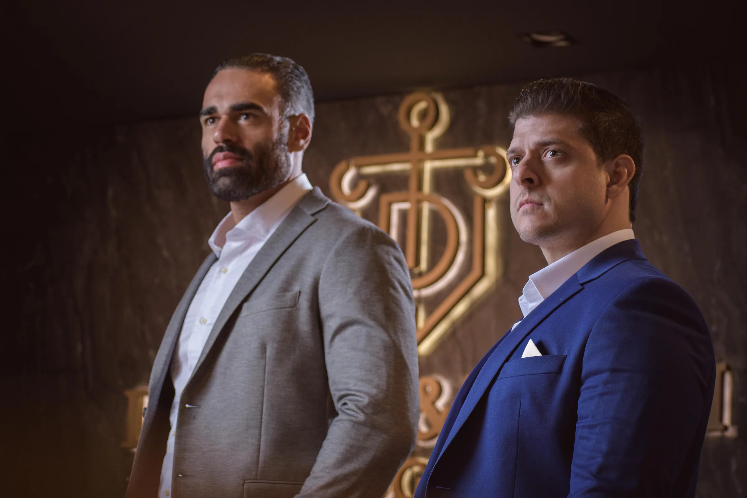 Os sócios Gustavo Dantas e Felipe Tadini diante do logotipo do escritório